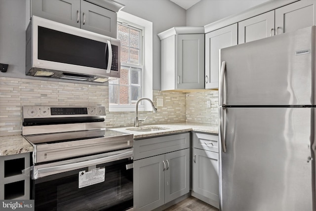 kitchen with light stone counters, a sink, gray cabinets, stainless steel appliances, and decorative backsplash