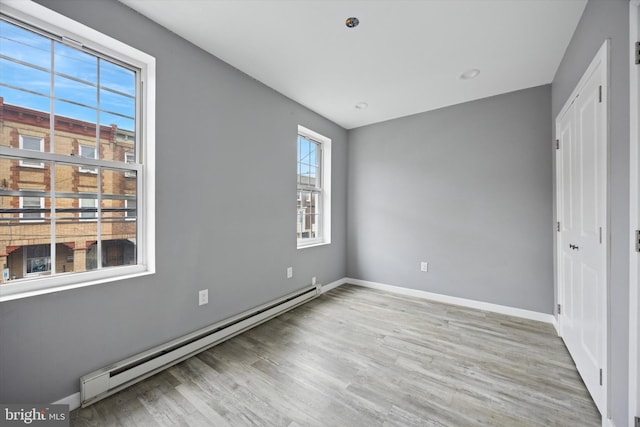 unfurnished bedroom featuring baseboards, a baseboard heating unit, and light wood-style flooring