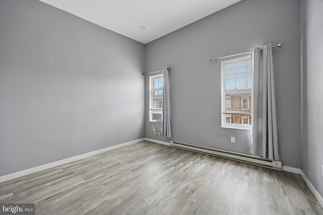 empty room featuring baseboards, a baseboard heating unit, and wood finished floors