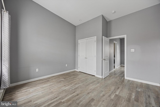 unfurnished bedroom featuring baseboards, high vaulted ceiling, wood finished floors, and a closet