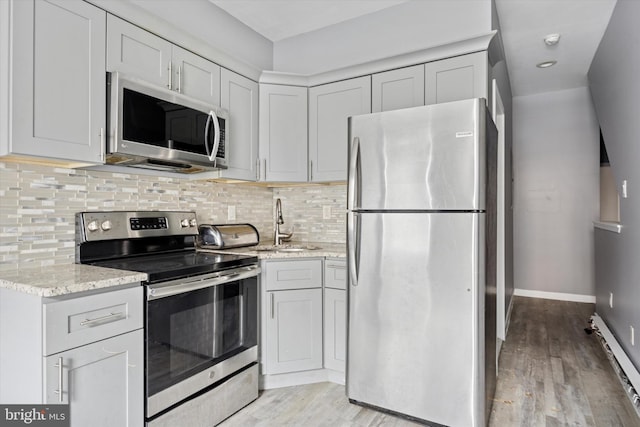 kitchen featuring stainless steel appliances, light stone counters, decorative backsplash, and light wood finished floors