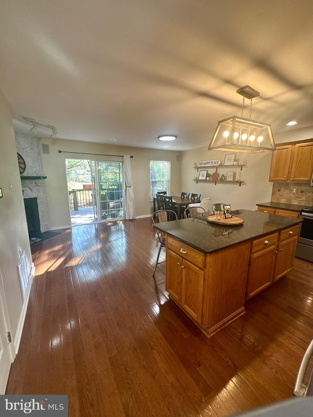 kitchen featuring dark wood-style flooring, a breakfast bar area, a stone fireplace, a center island, and open floor plan