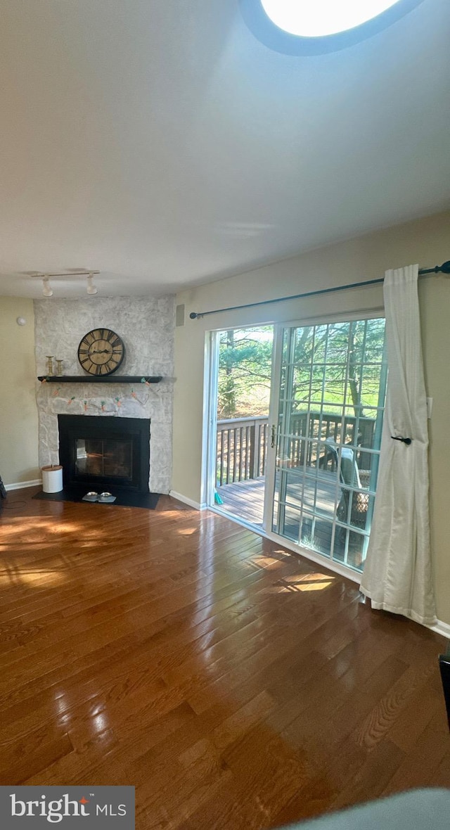 unfurnished living room with baseboards, a fireplace, hardwood / wood-style flooring, and rail lighting
