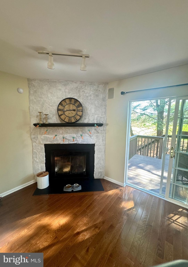 unfurnished living room with baseboards, track lighting, wood finished floors, and a fireplace