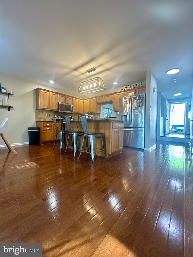kitchen with baseboards, a kitchen breakfast bar, brown cabinets, appliances with stainless steel finishes, and backsplash