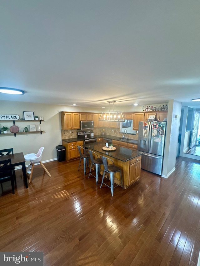 kitchen featuring a kitchen island, appliances with stainless steel finishes, tasteful backsplash, dark countertops, and a sink