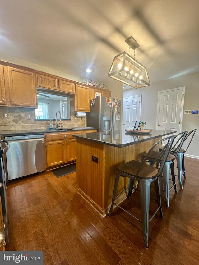 kitchen featuring appliances with stainless steel finishes, a sink, dark wood finished floors, a center island, and backsplash