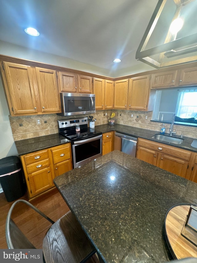 kitchen with a sink, appliances with stainless steel finishes, backsplash, and dark stone countertops