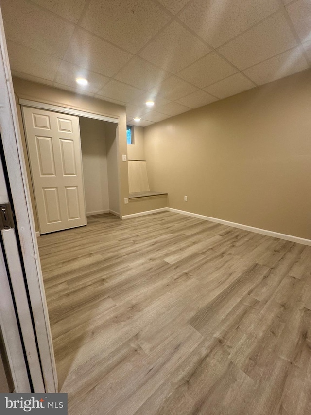 finished basement with recessed lighting, baseboards, a drop ceiling, and light wood-style floors