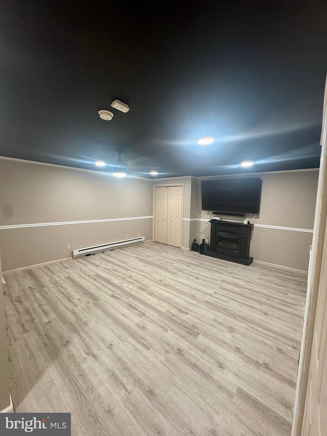 finished basement with a fireplace with raised hearth, baseboards, light wood-style flooring, and a baseboard radiator