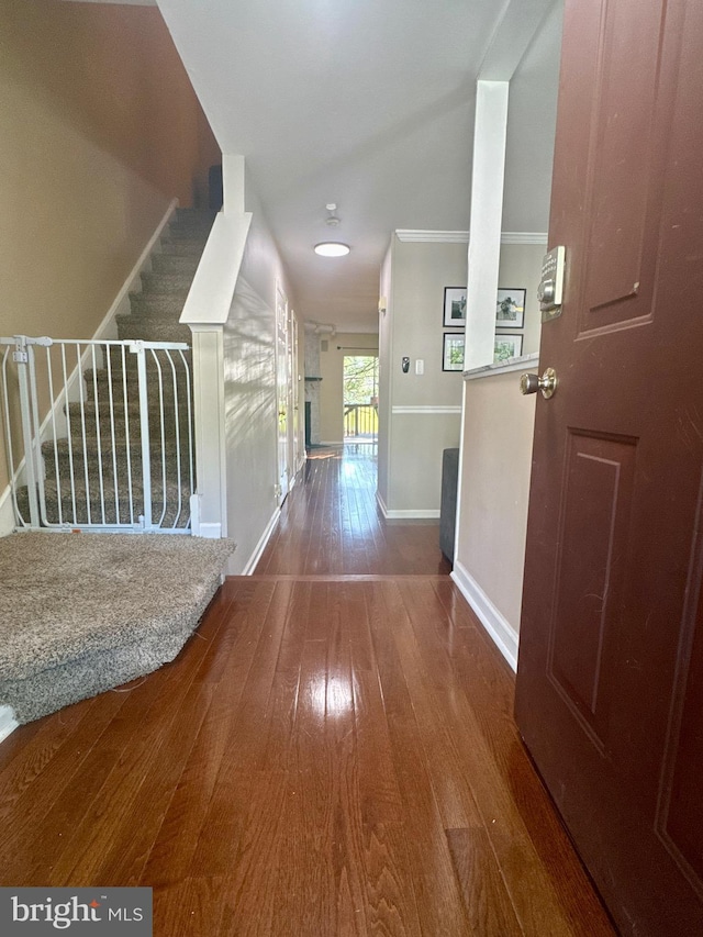 hallway with baseboards, crown molding, hardwood / wood-style flooring, and stairway