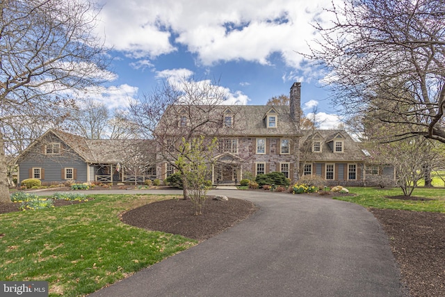 colonial inspired home with curved driveway, a chimney, stone siding, and a front lawn