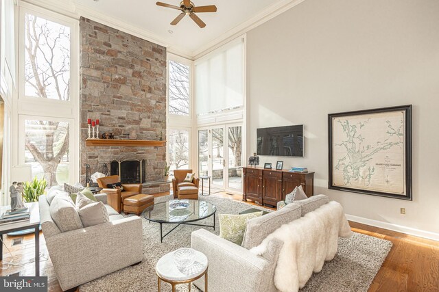 living room with crown molding, a ceiling fan, baseboards, wood finished floors, and a towering ceiling