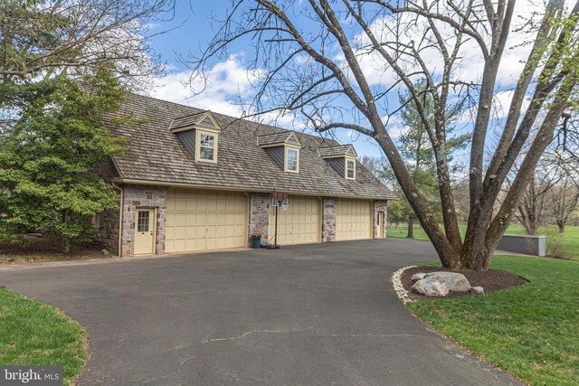 cape cod house with a front lawn, driveway, and stone siding