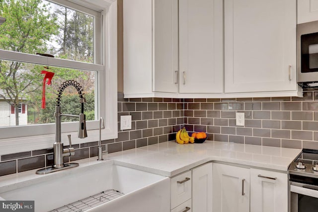 kitchen with a sink, white cabinetry, stainless steel microwave, decorative backsplash, and range with electric stovetop