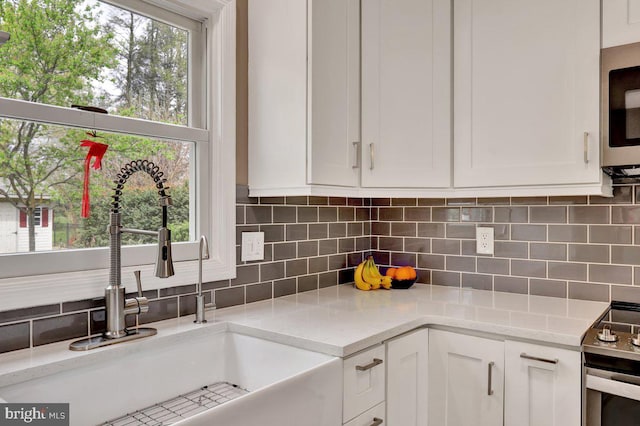 kitchen featuring decorative backsplash, range with electric cooktop, a sink, white cabinets, and stainless steel microwave