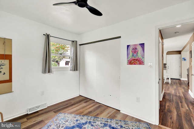 unfurnished bedroom featuring visible vents, a closet, wood finished floors, baseboards, and a ceiling fan