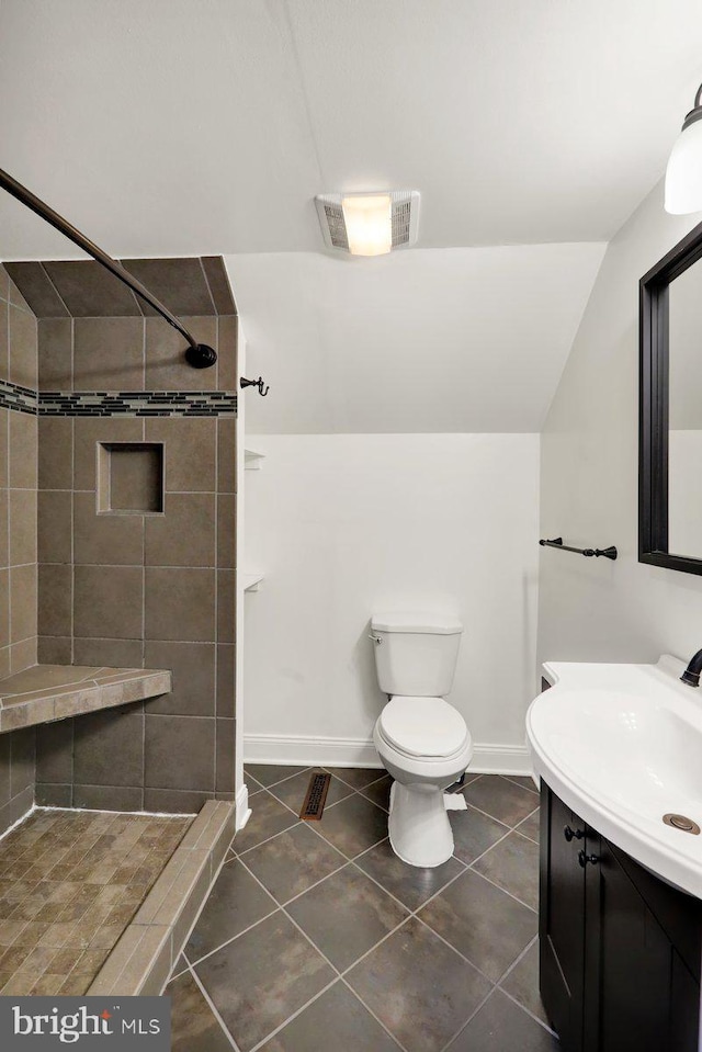 bathroom with toilet, baseboards, tiled shower, and vanity