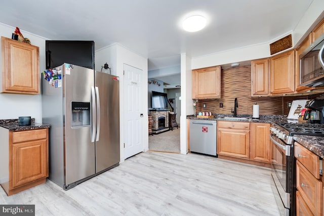 kitchen featuring decorative backsplash, light wood-style floors, a sink, dark stone countertops, and stainless steel appliances