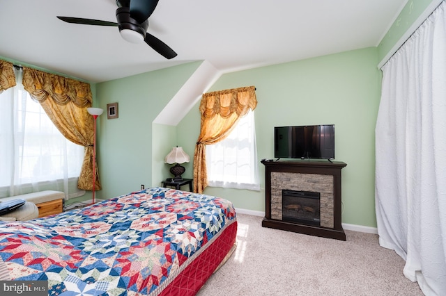 bedroom featuring multiple windows, carpet, a stone fireplace, and ceiling fan