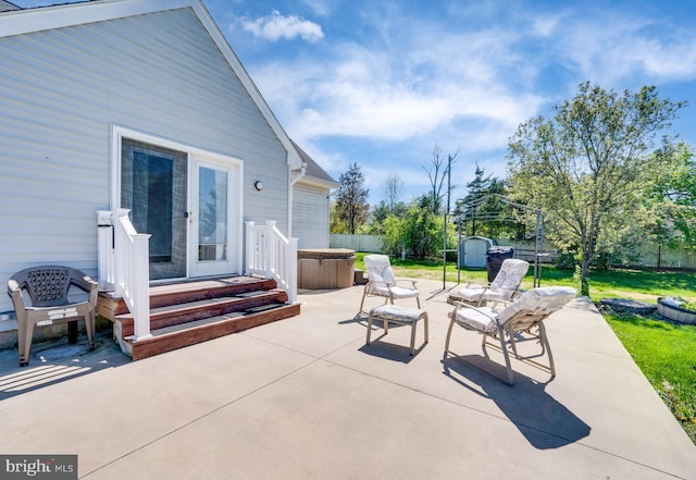 view of patio with a storage unit, a hot tub, fence, and an outbuilding