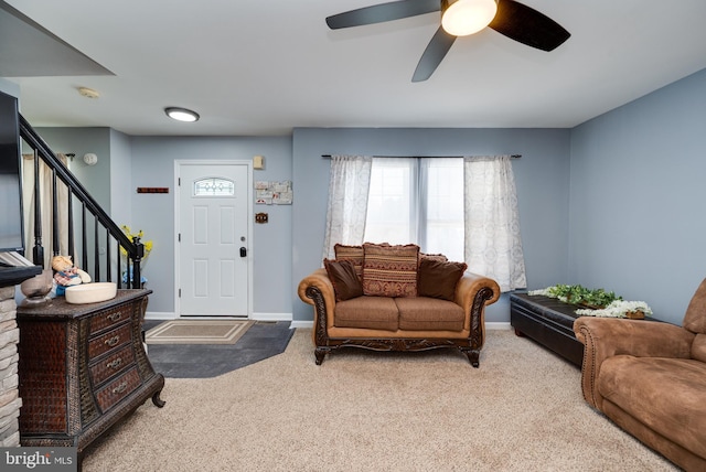 living room featuring carpet floors, baseboards, a ceiling fan, and stairs