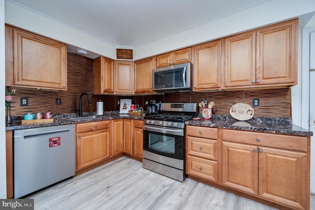 kitchen with a sink, dark stone countertops, appliances with stainless steel finishes, and tasteful backsplash