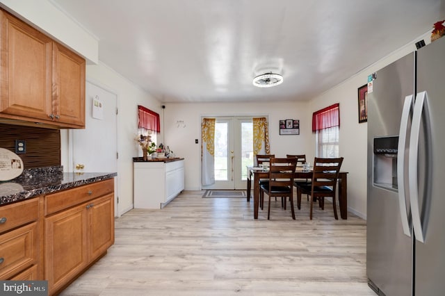 kitchen with brown cabinetry, french doors, stainless steel refrigerator with ice dispenser, dark stone countertops, and light wood finished floors