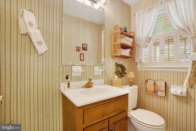half bath with vanity, toilet, and wallpapered walls