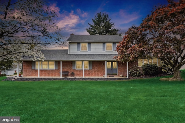 traditional home featuring a chimney, french doors, roof with shingles, a lawn, and brick siding