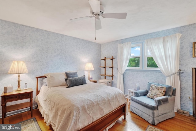 bedroom featuring ceiling fan, wood finished floors, and wallpapered walls
