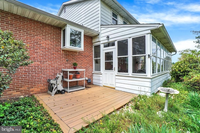 rear view of house featuring a wooden deck, a sunroom, and brick siding