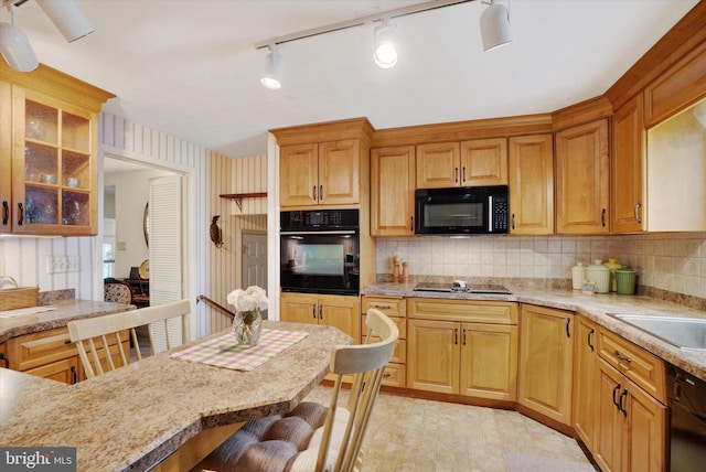 kitchen featuring glass insert cabinets, a breakfast bar area, wallpapered walls, backsplash, and black appliances