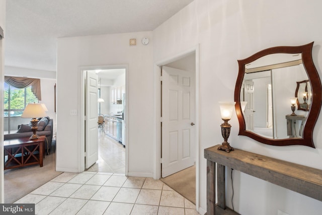 corridor with light tile patterned flooring, baseboards, and light carpet