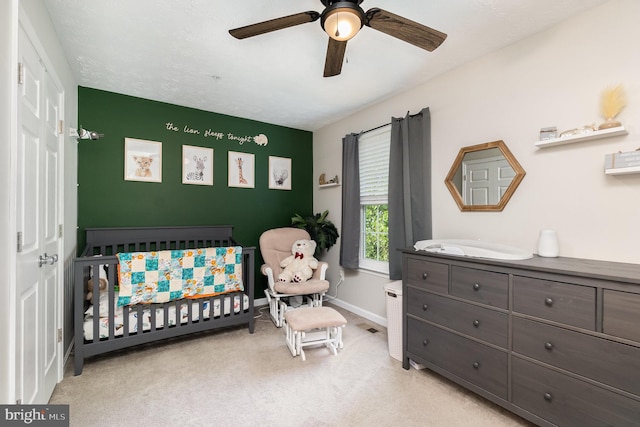 bedroom with baseboards, a ceiling fan, a nursery area, and light carpet