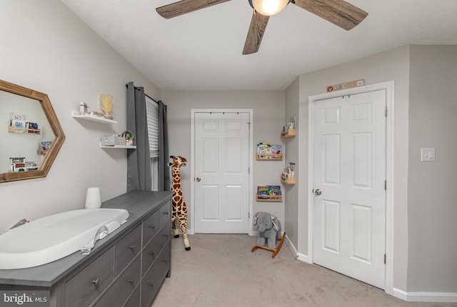 interior space with a sink, baseboards, ceiling fan, and light colored carpet