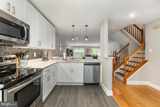 kitchen with wood finished floors, a sink, baseboards, stainless steel appliances, and white cabinetry