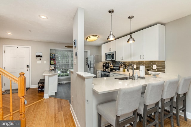kitchen featuring appliances with stainless steel finishes, a sink, light countertops, wood finished floors, and backsplash