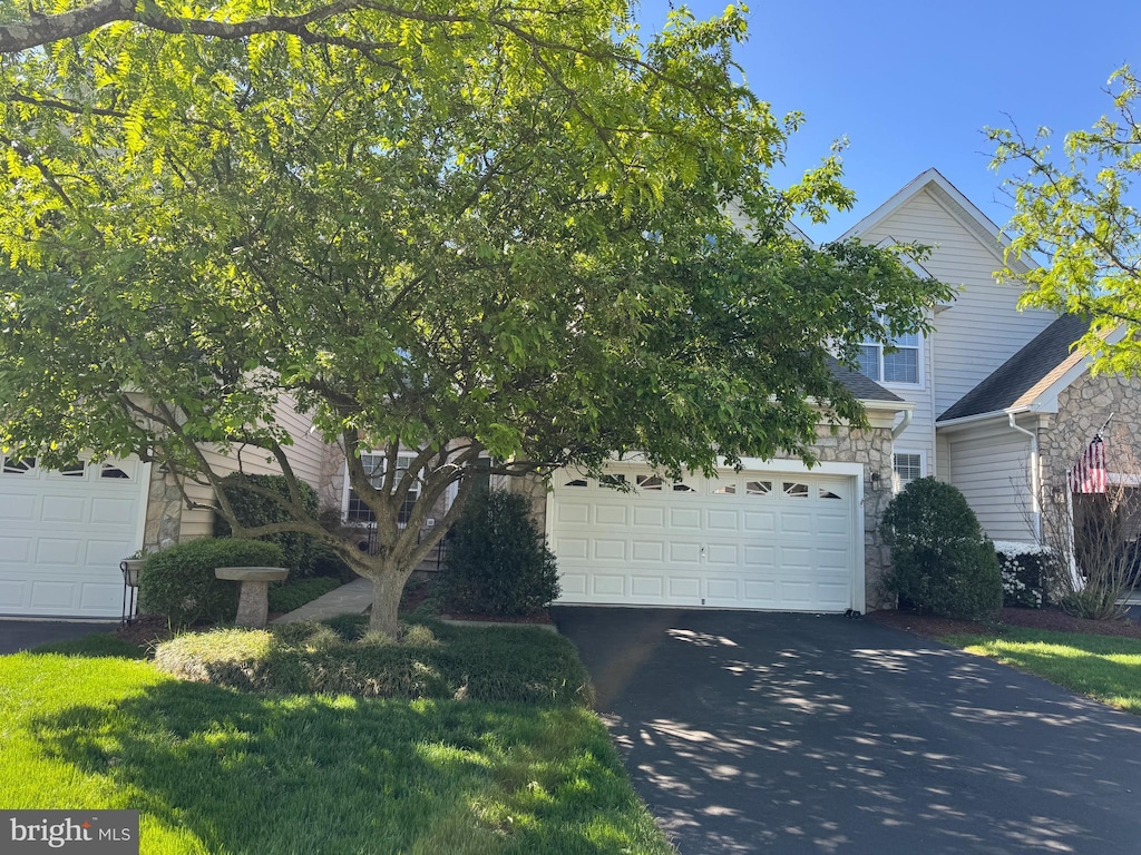 view of property hidden behind natural elements featuring driveway, stone siding, and a garage