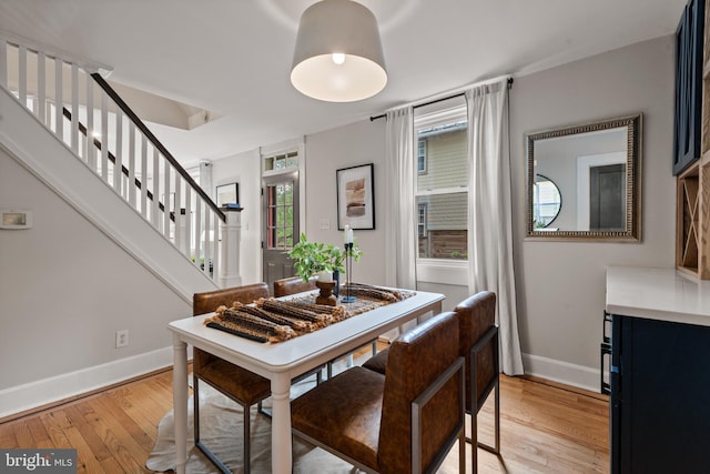 dining space with baseboards, light wood-type flooring, and stairs