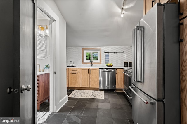 kitchen with appliances with stainless steel finishes, light countertops, tasteful backsplash, dark tile patterned flooring, and a sink