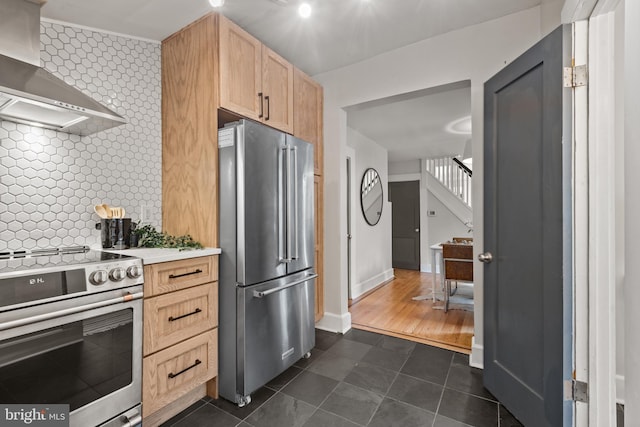 kitchen with appliances with stainless steel finishes, dark tile patterned floors, light brown cabinetry, wall chimney range hood, and light countertops