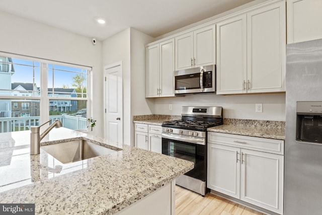 kitchen with light stone countertops, a sink, stainless steel appliances, recessed lighting, and white cabinetry