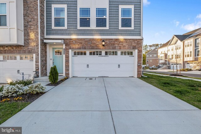 view of front facade with an attached garage, a residential view, driveway, and stone siding