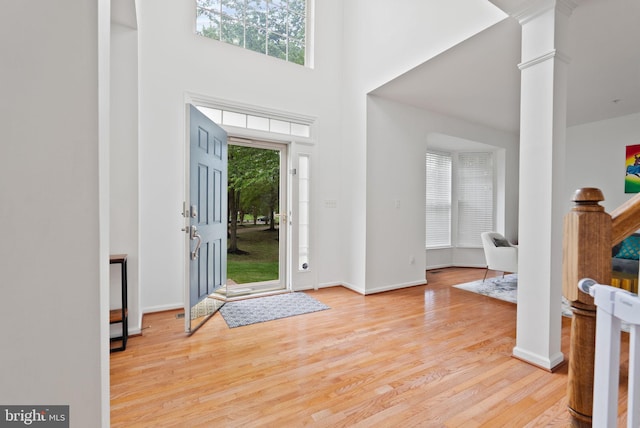 entrance foyer featuring ornate columns, baseboards, wood finished floors, and a towering ceiling