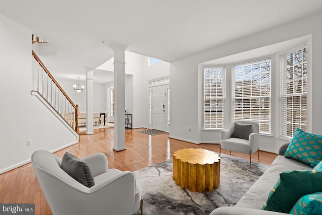 living room featuring stairs, decorative columns, wood finished floors, baseboards, and a notable chandelier