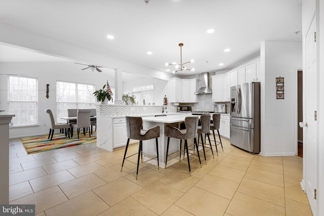 kitchen featuring decorative backsplash, a breakfast bar area, wall chimney range hood, stainless steel fridge, and white cabinets