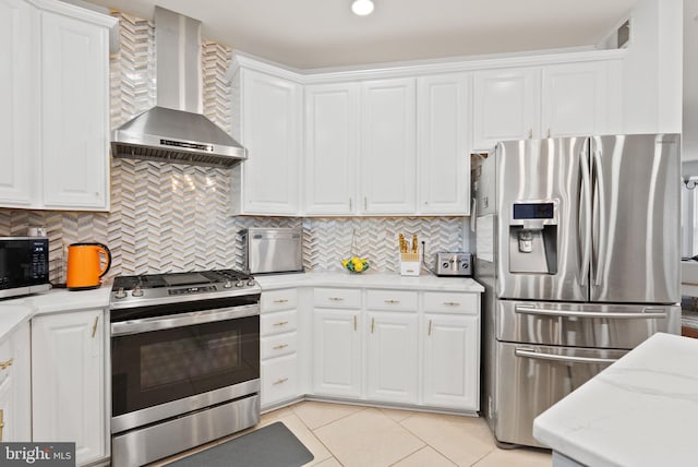 kitchen featuring light tile patterned floors, white cabinets, stainless steel appliances, and wall chimney exhaust hood