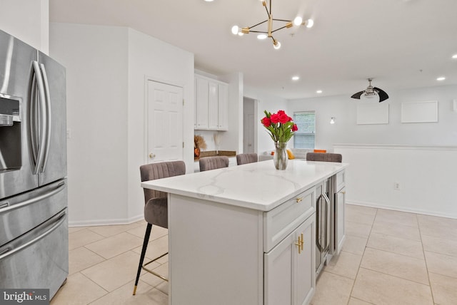 kitchen with a breakfast bar area, stainless steel refrigerator with ice dispenser, white cabinets, light stone counters, and light tile patterned floors
