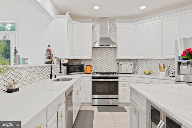 kitchen with wall chimney range hood, backsplash, a sink, stainless steel appliances, and white cabinetry